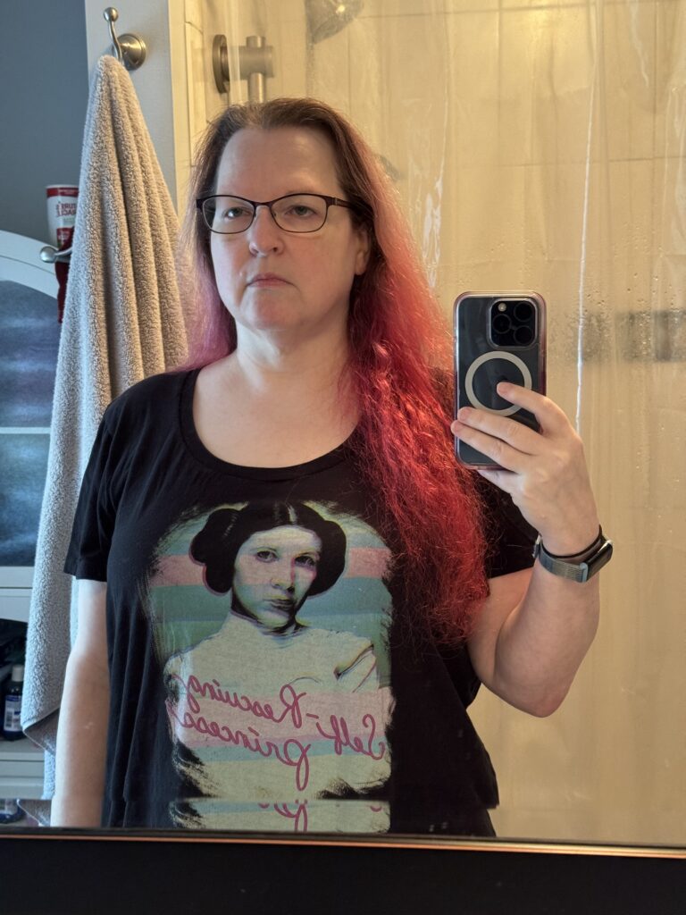 Same woman, wearing the same shirt. Bright red hair loose over her shoulder. She's noticeably thinner and the shirt is almost baggy in places.