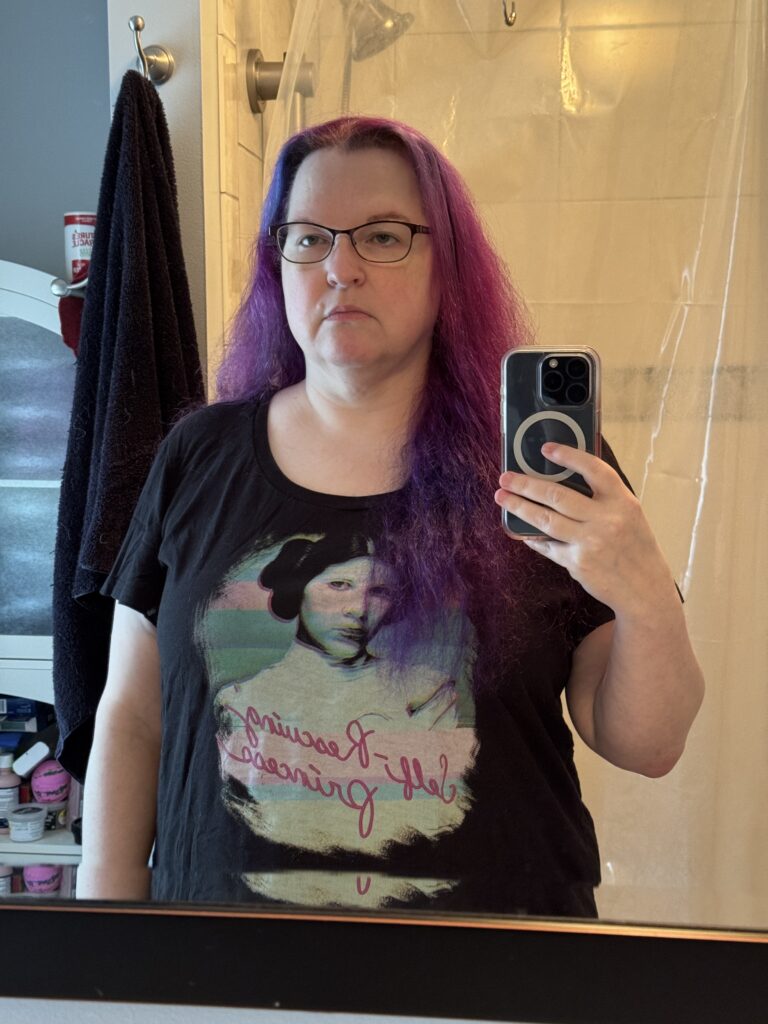 The same woman, wearing the same shirt, with hair loose, fuchsia fading to purple. Her face is a bit thinner, the shirt is a bit looser.
